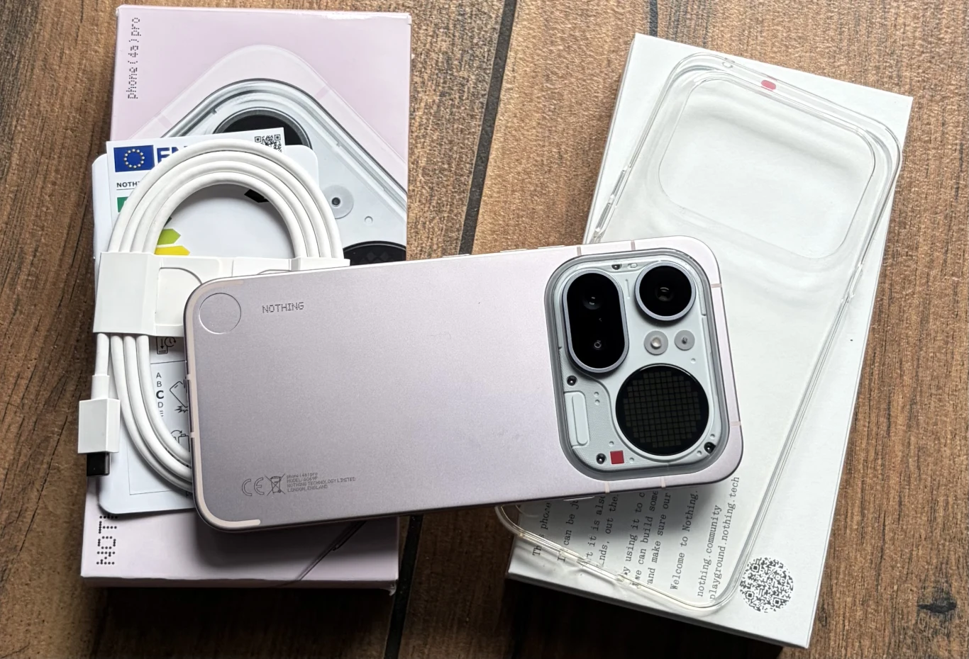 smartfon marki Nothing Phone 2a w jasnej obudowie, położony na oryginalnym pudełku z widocznymi akcesoriami takimi jak przezroczyste etui i kabel USB typu C oraz dokumentacja