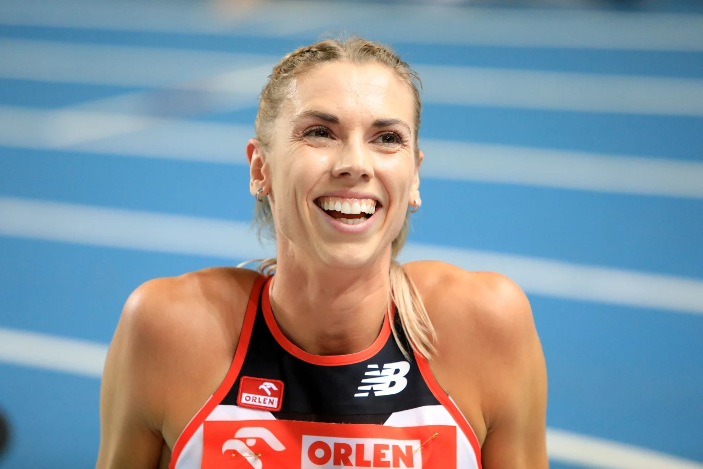 uśmiechnięta lekkoatletka w stroju sportowym z logo ORLEN na tle bieżni lekkoatletycznej