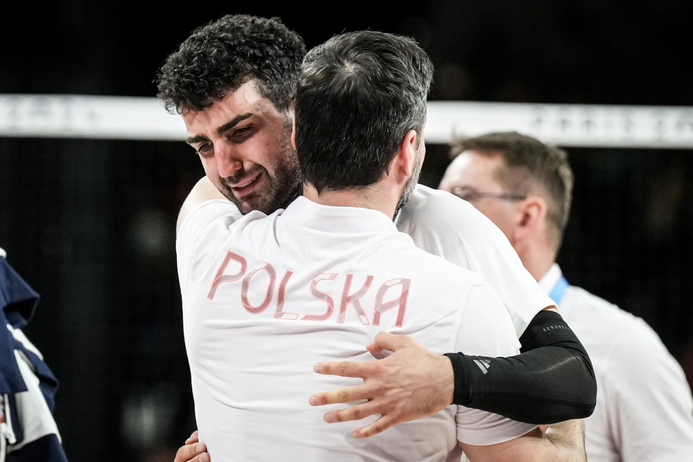 dwóch mężczyzn w koszulkach z napisem „Polska” obejmuje się w geście wsparcia i emocji na tle sportowej hali