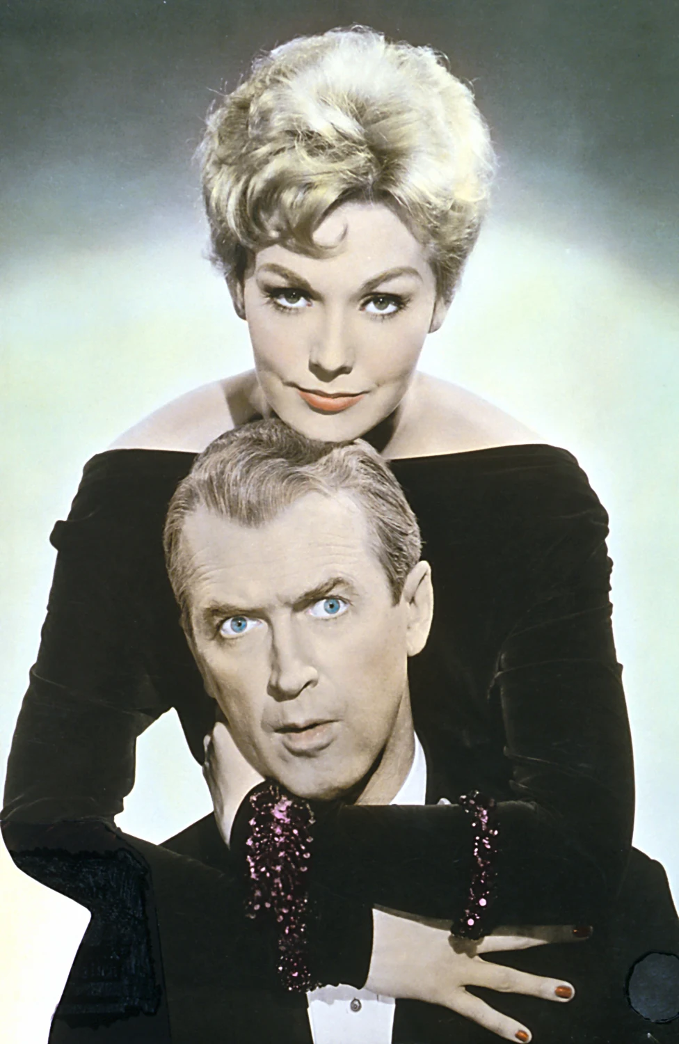 kobieta o krótkich, blond włosach ubrana w czarną, elegancką suknię obejmuje mężczyznę o jasnych oczach i siwych włosach, oboje patrzą prosto przed siebie z poważnym wyrazem twarzy