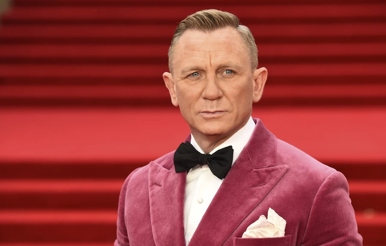 Daniel Craig Daniel Craig w różowym aksamitnym smokingu, białej koszuli i czarnej muszce na tle czerwonych schodów