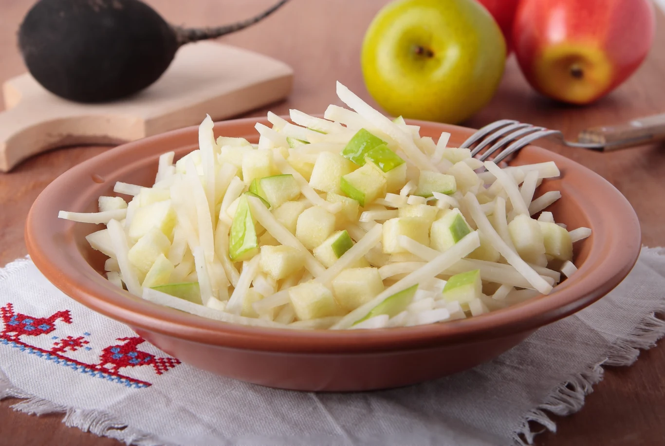 Surowy seler powinno być stałe wpisany w menu osób po 50. i 60. roku życia. Sałatka z pokrojonego selera i jabłka w brązowej misce na lnianej serwetce z czerwonym haftem.