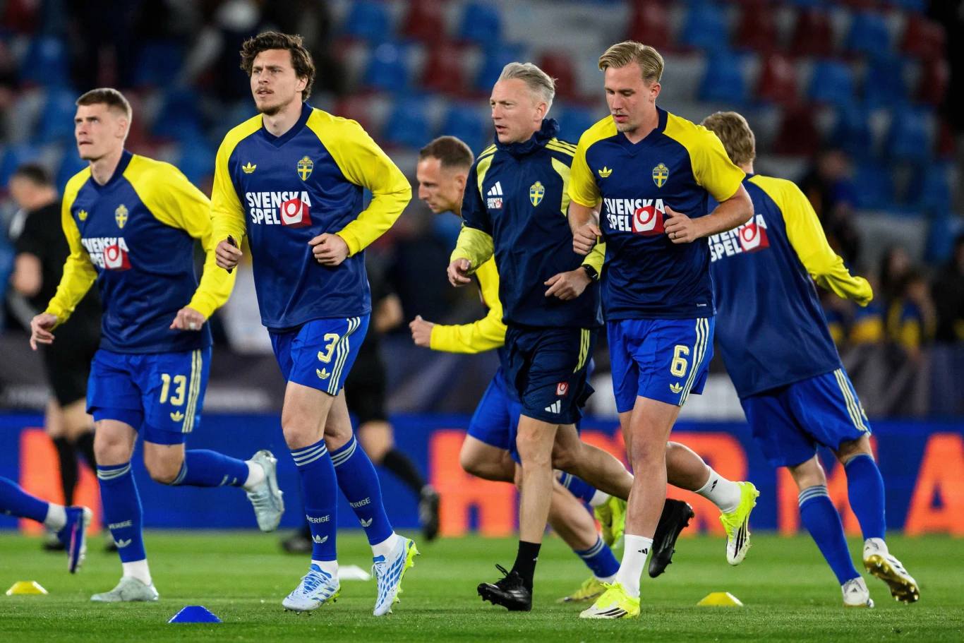 szwedzcy piłkarze w niebiesko-żółtych strojach podczas wspólnej rozgrzewki na stadionie, skupieni na ćwiczeniach biegowych