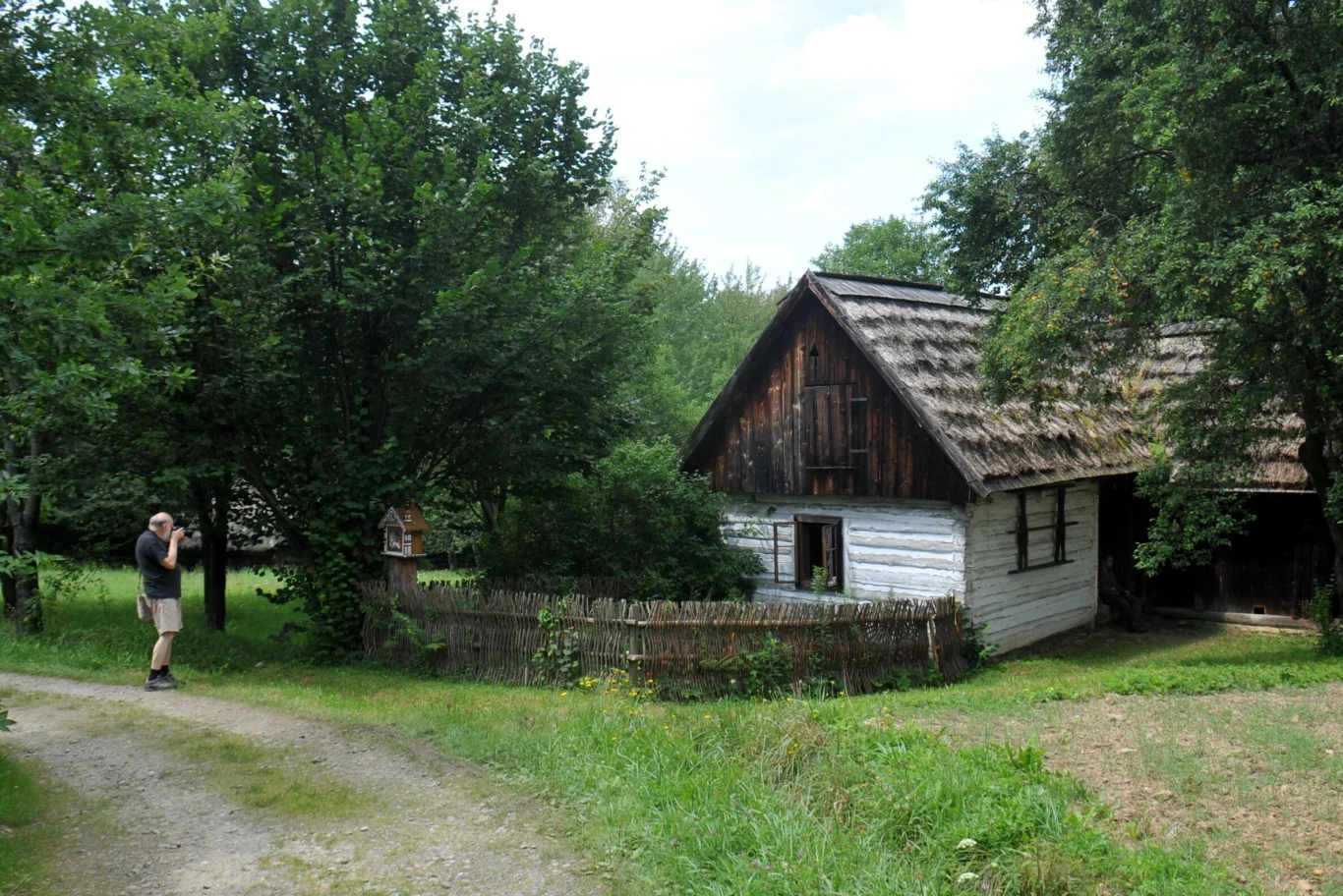 Jeden z najpiękniejszych skansenów w Polsce. Idealny cel na wiosenną wycieczkę. Drewniany budynek, jeden ze zgromadzonych w Sądeckim Parku Etnograficznym. Obok mężczyzna fotografuje budynek.