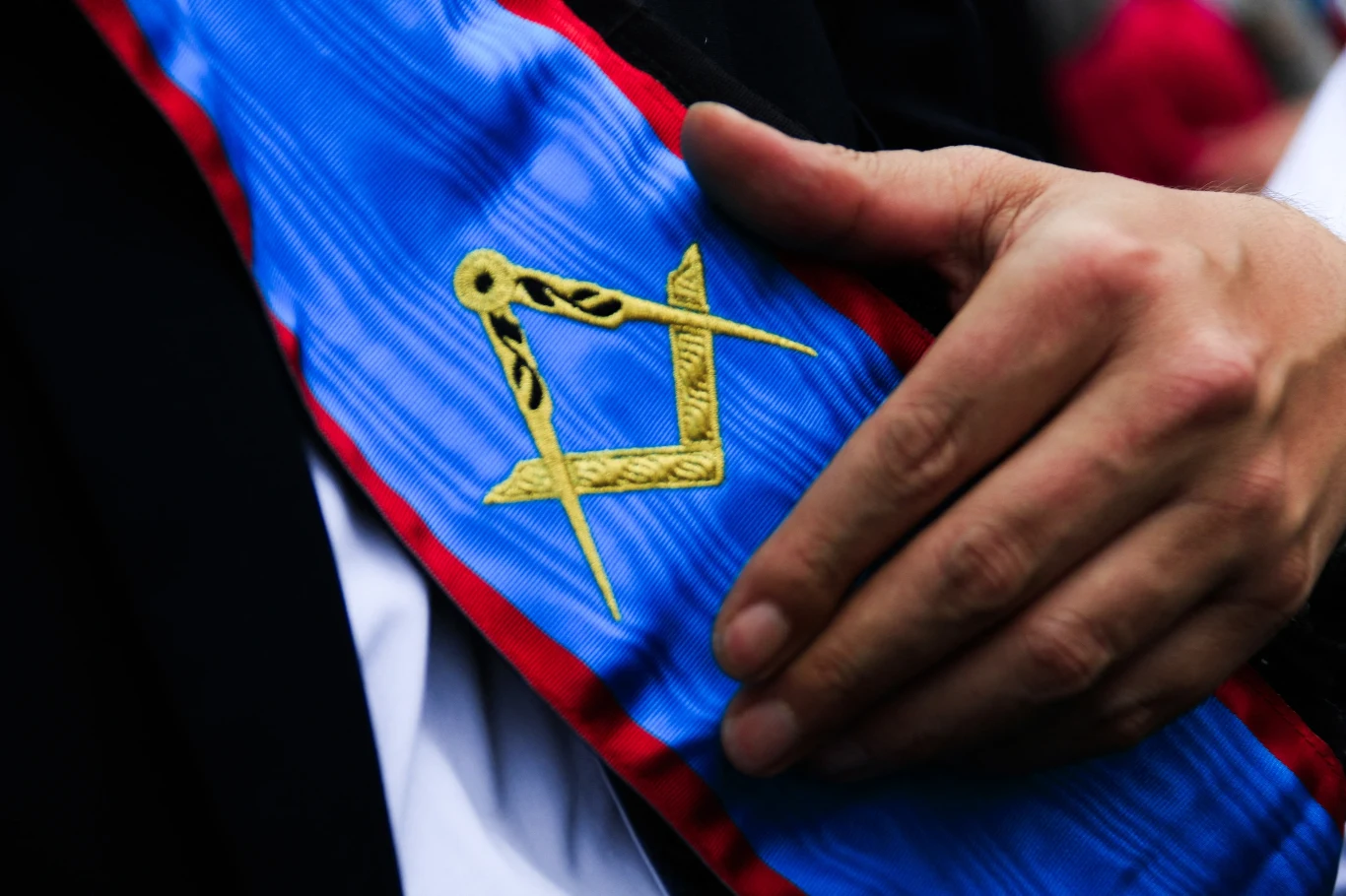 Zdj. ilustracyjne. W Paryżu rusza proces 22 podejrzanych o współpracę przestępczą z masonerią Niebieska szarfa z czerwonymi brzegami i złotym symbolem cyrkla i węgielnicy (masoneria) w dłoni w garniturze.