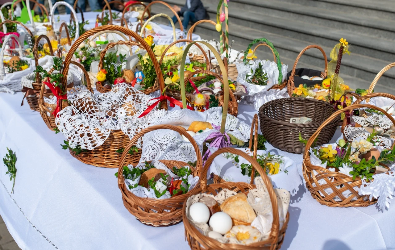 Wielka Sobota i święcenie pokarmów Koszyki wielkanocne z jajkami, chlebem i kiełbasą na białym obrusie, ozdobione serwetkami i bukszpanem.