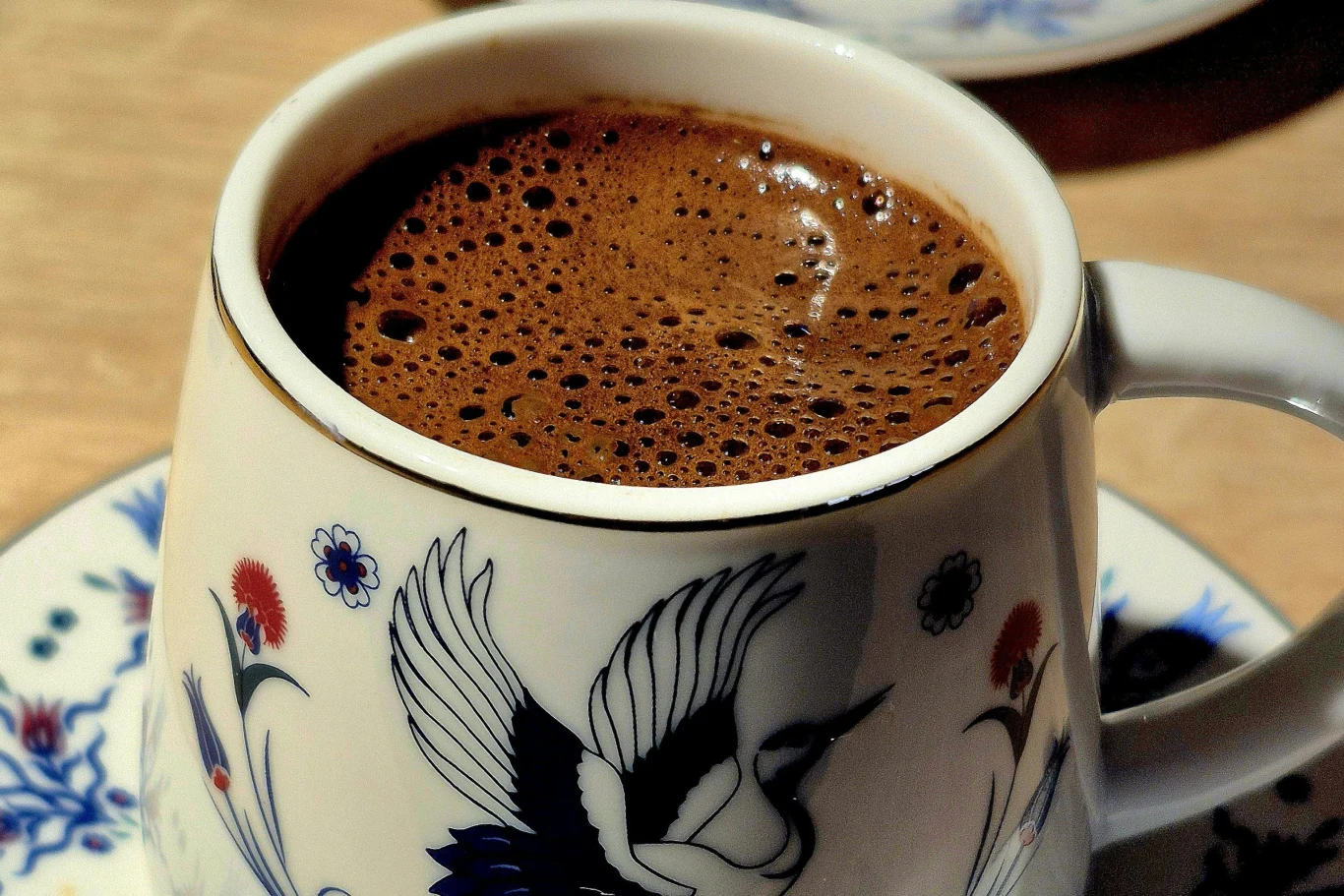 Kawa z solą może wesprzeć organizm Filiżanka kawy z gęstą pianką, ozdobiona motywem ptaka, na tle kolorowych kwiatów.