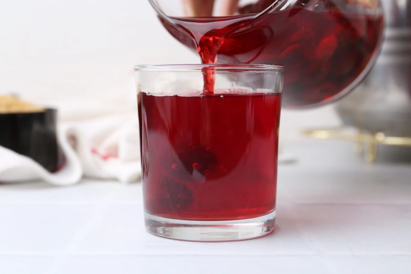 Sok z popularnych owoców chroni przed osteoporozą i miażdżycą, reguluje pracę jelit. Klarowny, czerwony sok owocowy nalewany z dzbanka do szklanki z kawałkami owoców zanurzonymi w płynie.