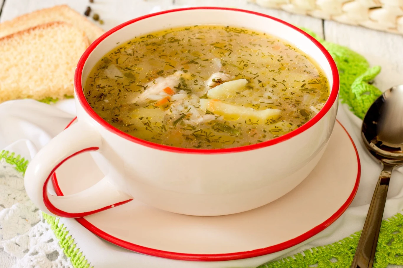 Pyszny i zdrowy krupnik to świetny pomysł na obiad Miska krupniku z warzywami, kaszą, koperkiem, obok kromka chleba i łyżka na zielonej serwetce