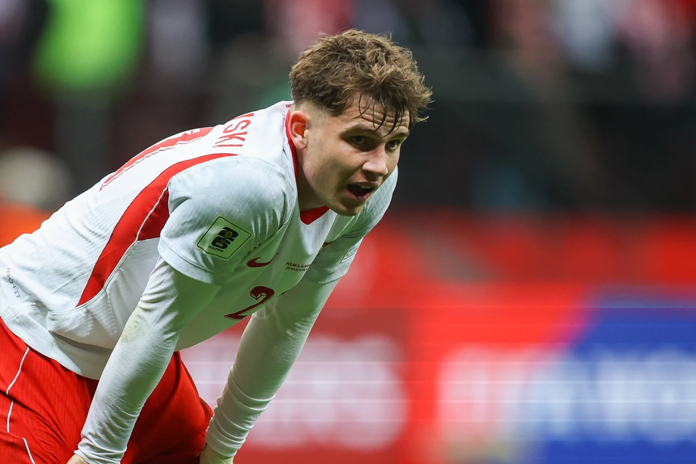 piłkarz w biało-czerwonym stroju z numerem 2 na plecach pochylony do przodu na boisku, wyczerpany po wysiłku sportowym