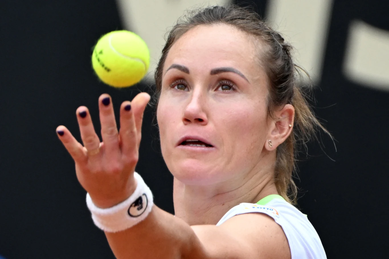 kobieta w białym stroju sportowym przygotowuje się do serwisu podczas meczu tenisowego, skupiona na unoszącej się w powietrzu piłce tenisowej