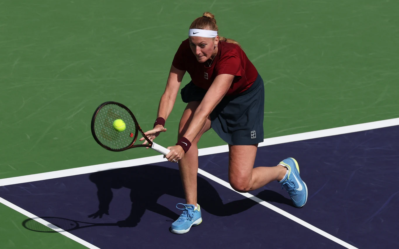 tenisistka w bordowej koszulce i niebieskich butach wykonuje uderzenie z bekhendu na twardym korcie, skupienie w jej oczach, piłka tenisowa tuż obok rakiety