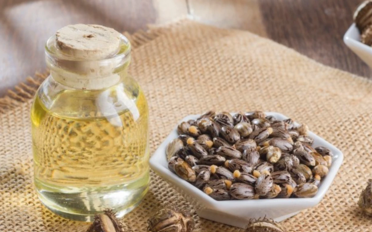 Butelka z jasnym olejem zamknięta korkiem oraz miseczka wypełniona ciemnymi nasionami rącznika ustawione na jutowym materiale.