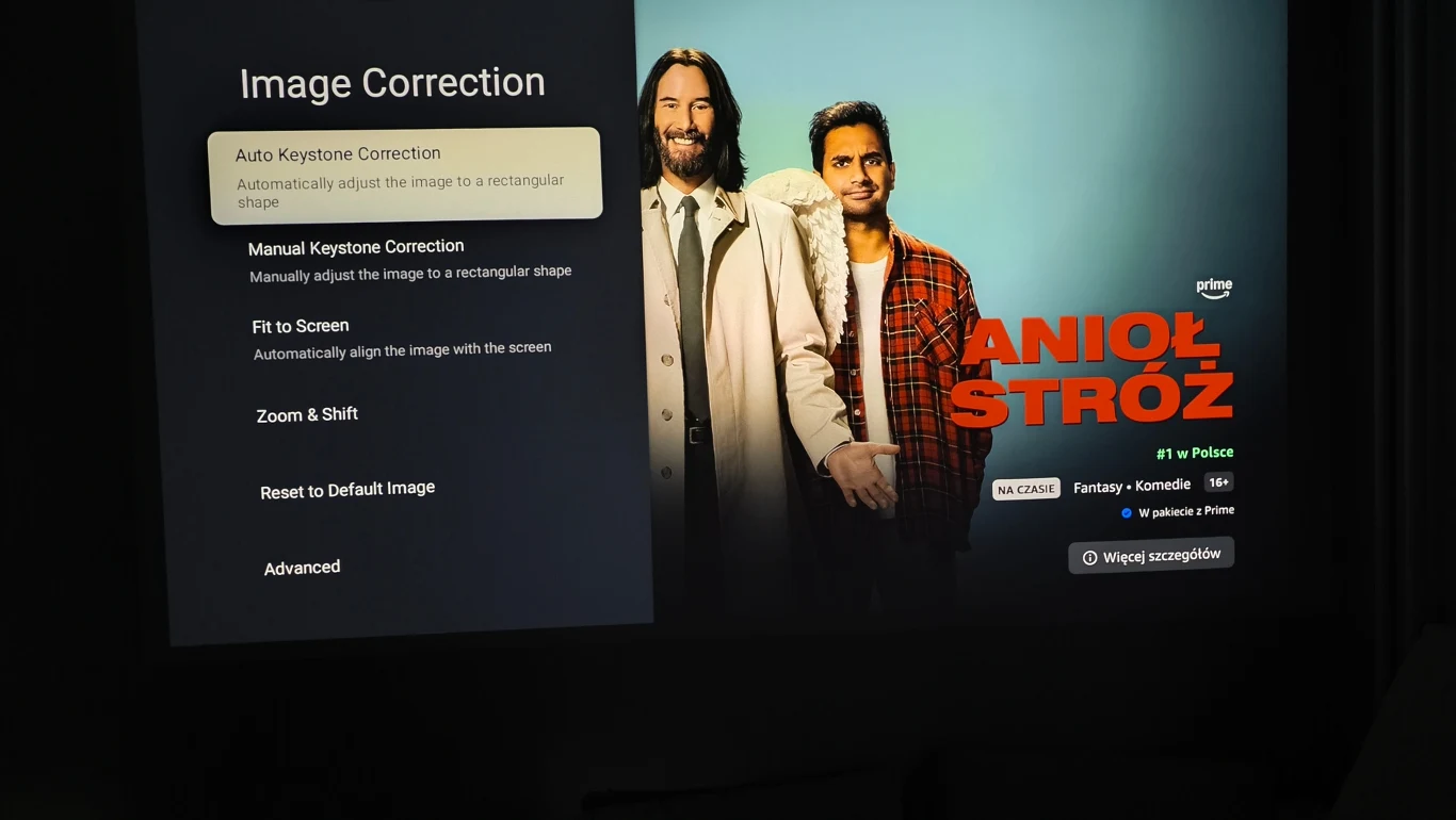 Interfejs korekcji obrazu z opcją automatycznej korekcji trapezu po lewej stronie oraz ekran startowy filmu „Anioł Stróż” z dwoma mężczyznami stojącymi na jasnym tle po prawej stronie.