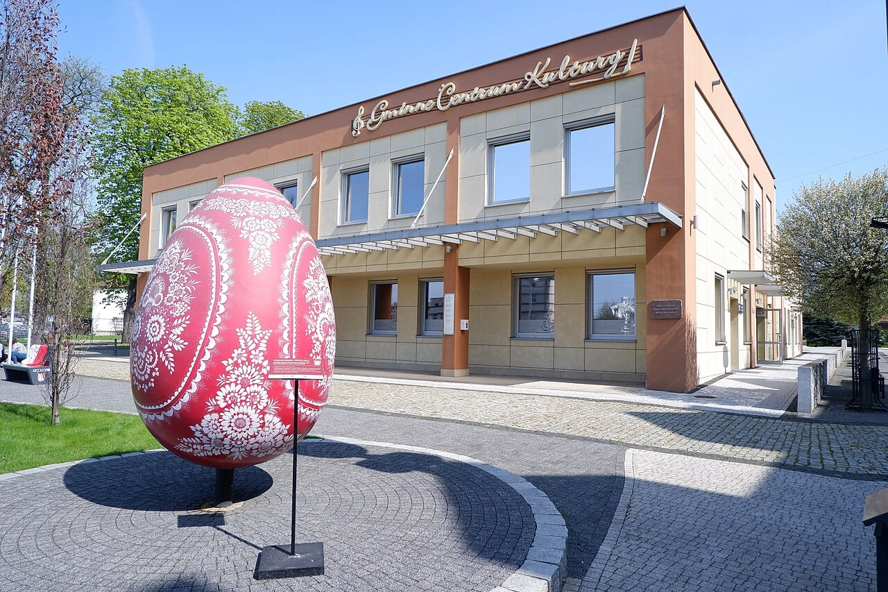 duża ozdobna pisanka w czerwono-białych barwach z tradycyjnymi wzorami stojąca przed budynkiem Gminnego Centrum Kultury