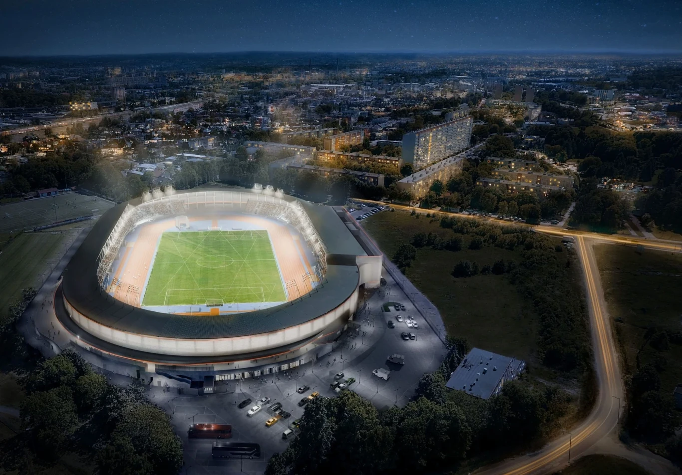 oświetlony stadion piłkarski podczas wieczornego meczu, wypełnione trybuny, zielona murawa, otaczające go parkingi z zaparkowanymi samochodami, w tle panoramę miasta rozświetlają miejskie światła