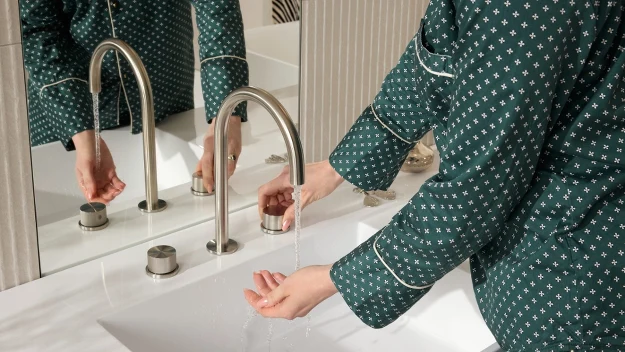osoba w zielonej piżamie myjąca ręce pod strumieniem wody z nowoczesnej baterii nad białą umywalką