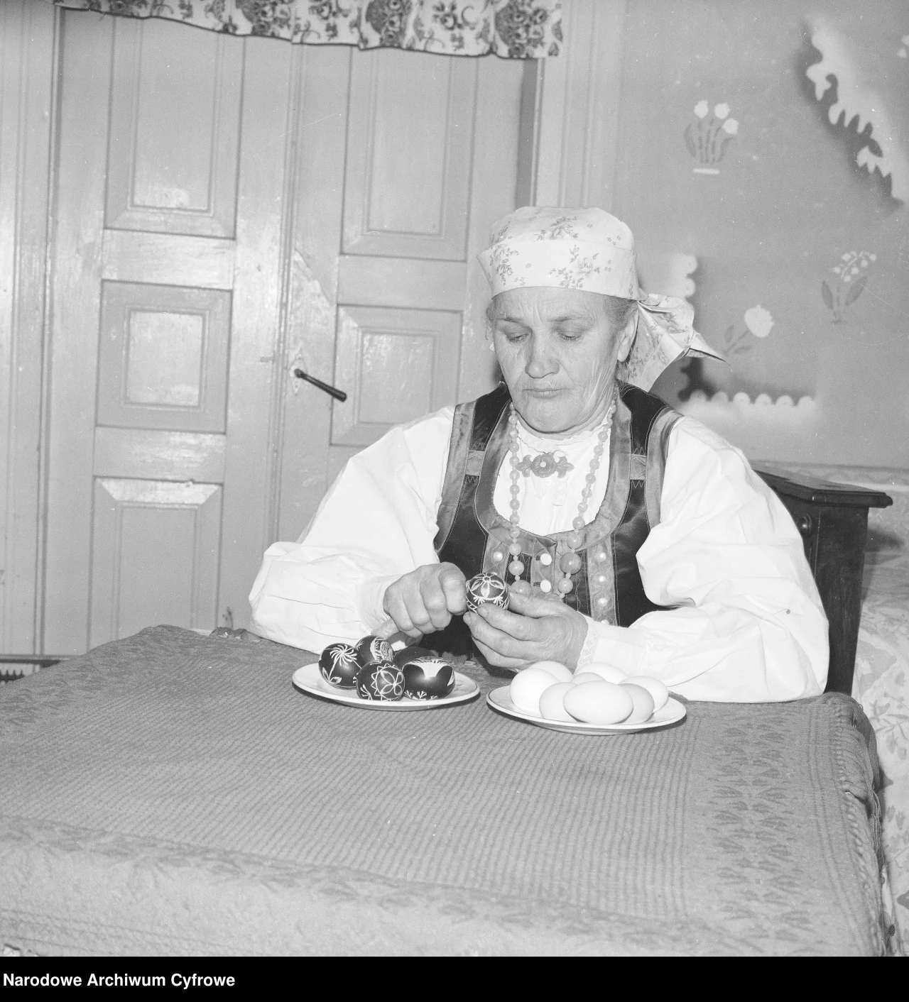 1976 rok: Kurpiowskie artystki ludowe w Kadzidle. Tradycja robienia pisanek przetrwała do dziś Starsza kobieta w tradycyjnym stroju ludowym maluje pisanki, siedząc przy stole, na którym leżą dekorowane i białe jajka.