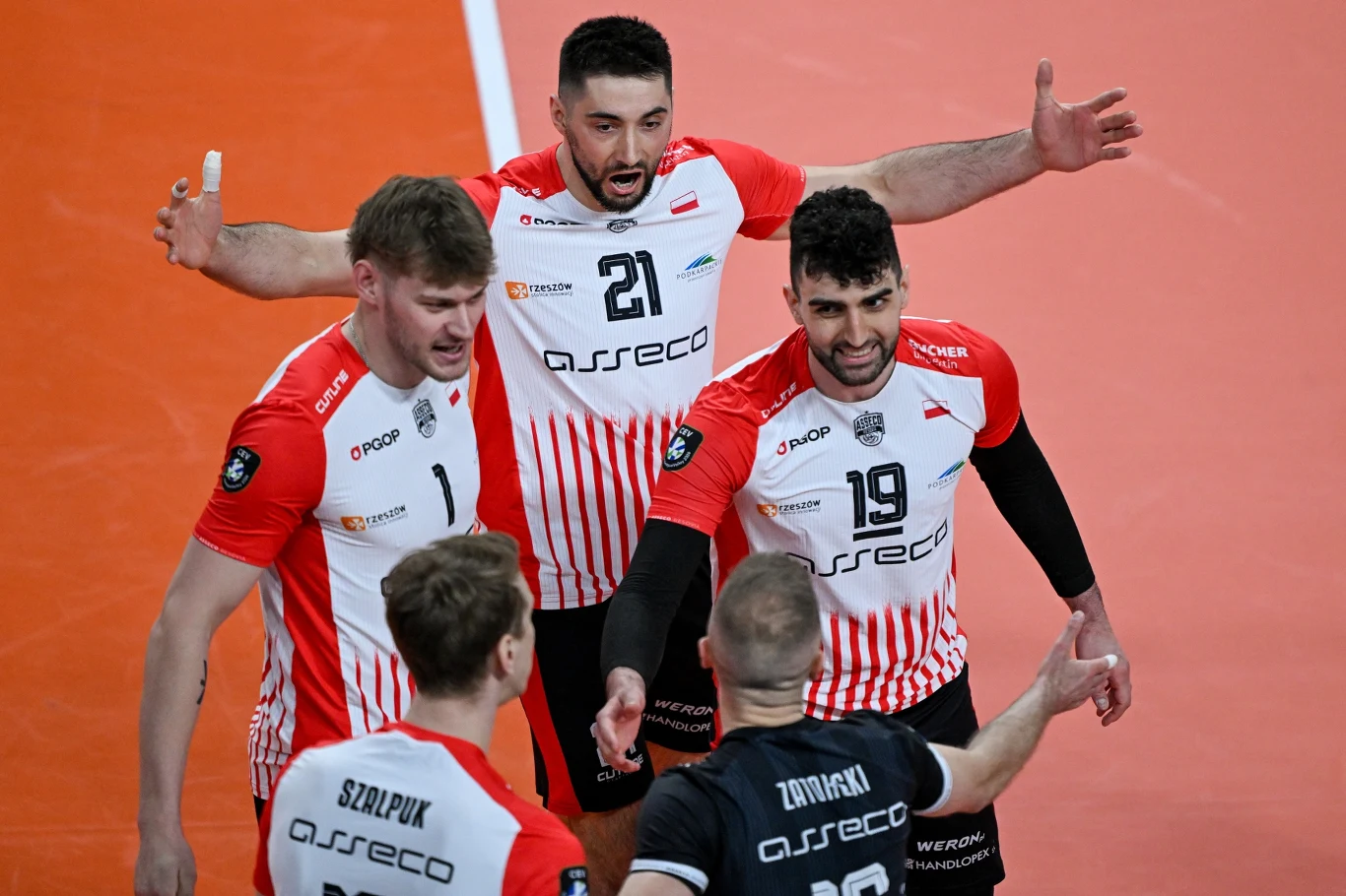 czterech siatkarzy w biało-czerwonych koszulkach drużyny Asseco Resovia świętuje zdobyty punkt, otaczając ramionami kolegę w czarnej koszulce z nazwiskiem na plecach, wszyscy skupieni na wspólnym geście zwycięstwa
