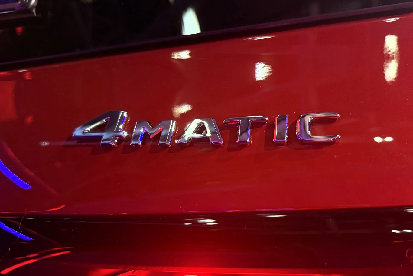 chromowany napis 4MATIC na tle czerwonej karoserii samochodu, odbijające się światła na błyszczącej powierzchni