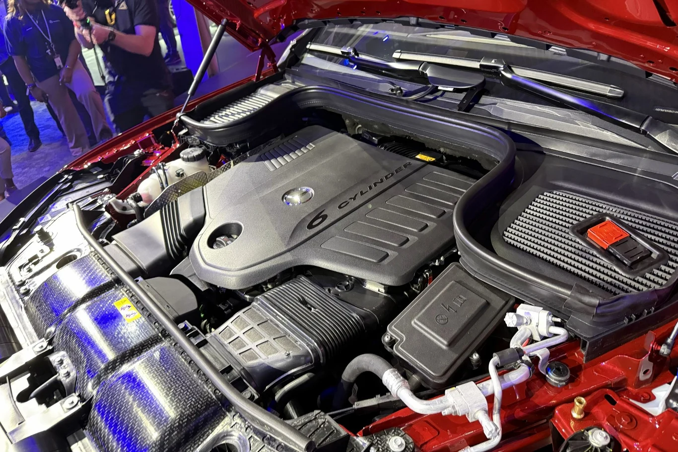 silnik samochodowy z osłoną oznaczoną napisem „6 CYLINDERS”, otoczony komponentami układu zasilania i przewodami, z widoczną komorą silnika w czerwonym nadwoziu