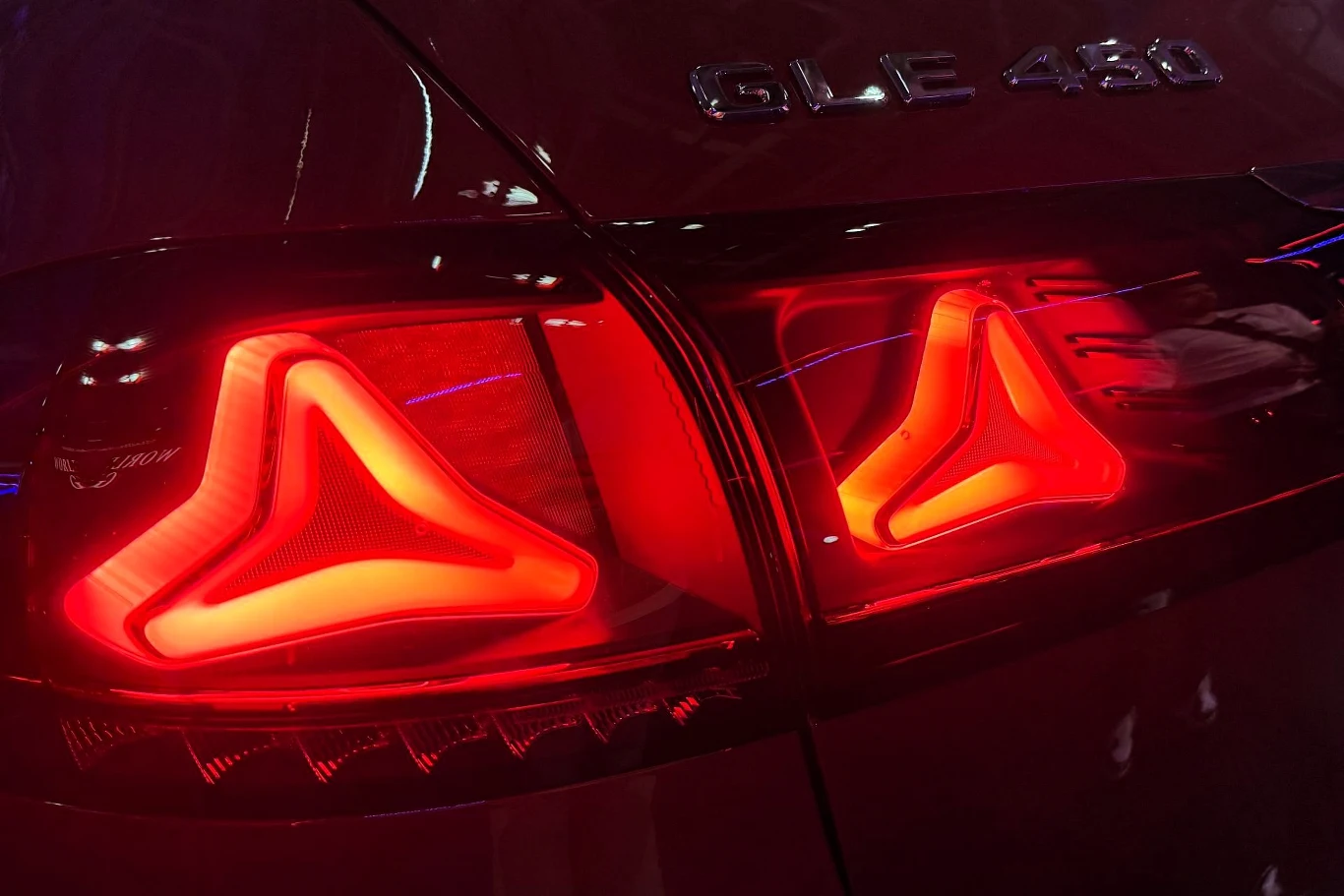 czerwone światła tylne samochodu Mercedes-Benz GLE 450 o charakterystycznym trójkątnym wzorze, intensywnie podświetlone na tle ciemnej karoserii z widocznym emblematem modelu