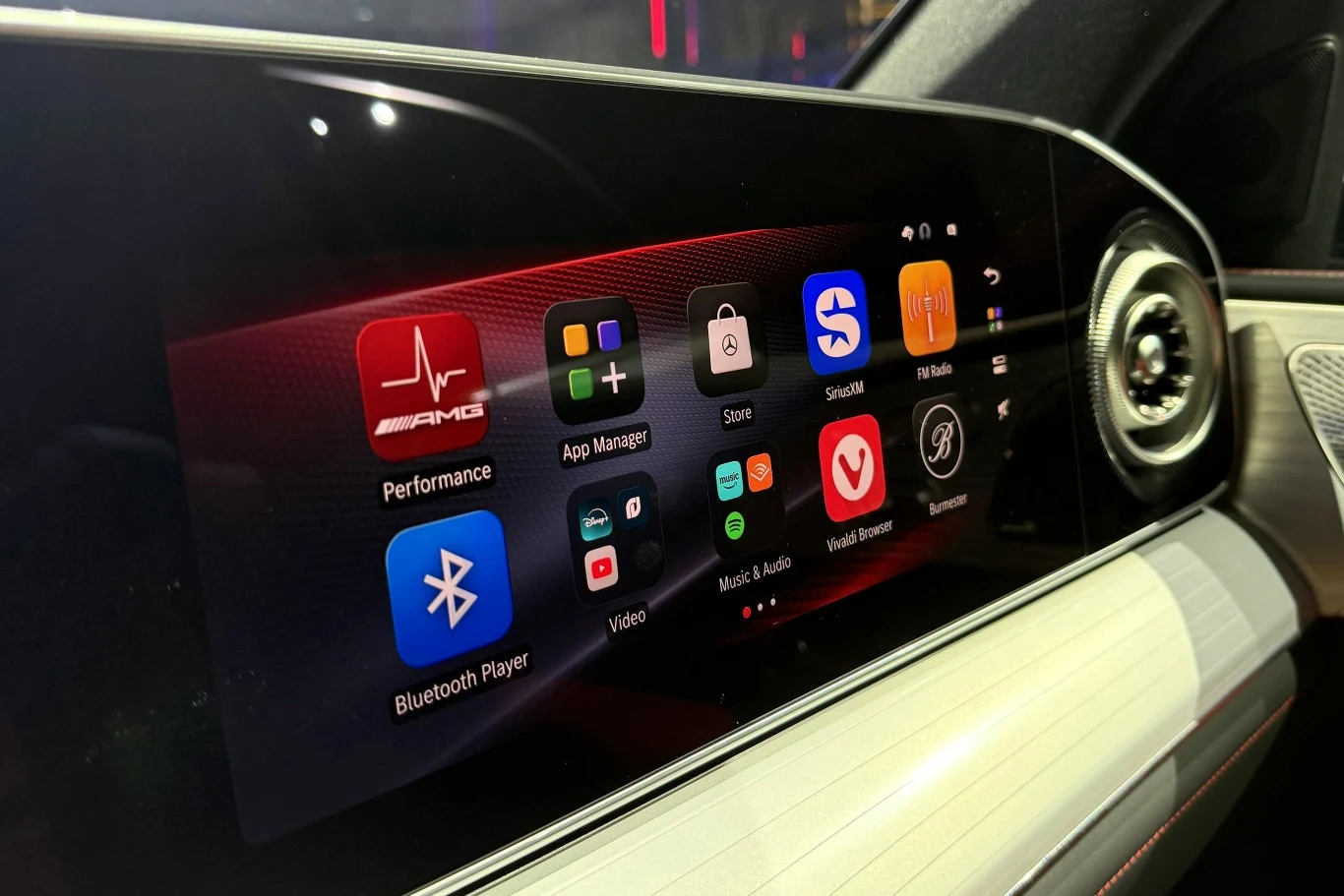 Dotykowy ekran systemu multimedialnego w samochodzie, wyświetlający kolorowe ikony aplikacji takich jak Bluetooth Player, Performance, App Manager, Youtube, przeglądarka internetowa czy Spotify, z jasnymi i wyraźnymi grafikami na tle czarno-czerwonego ...