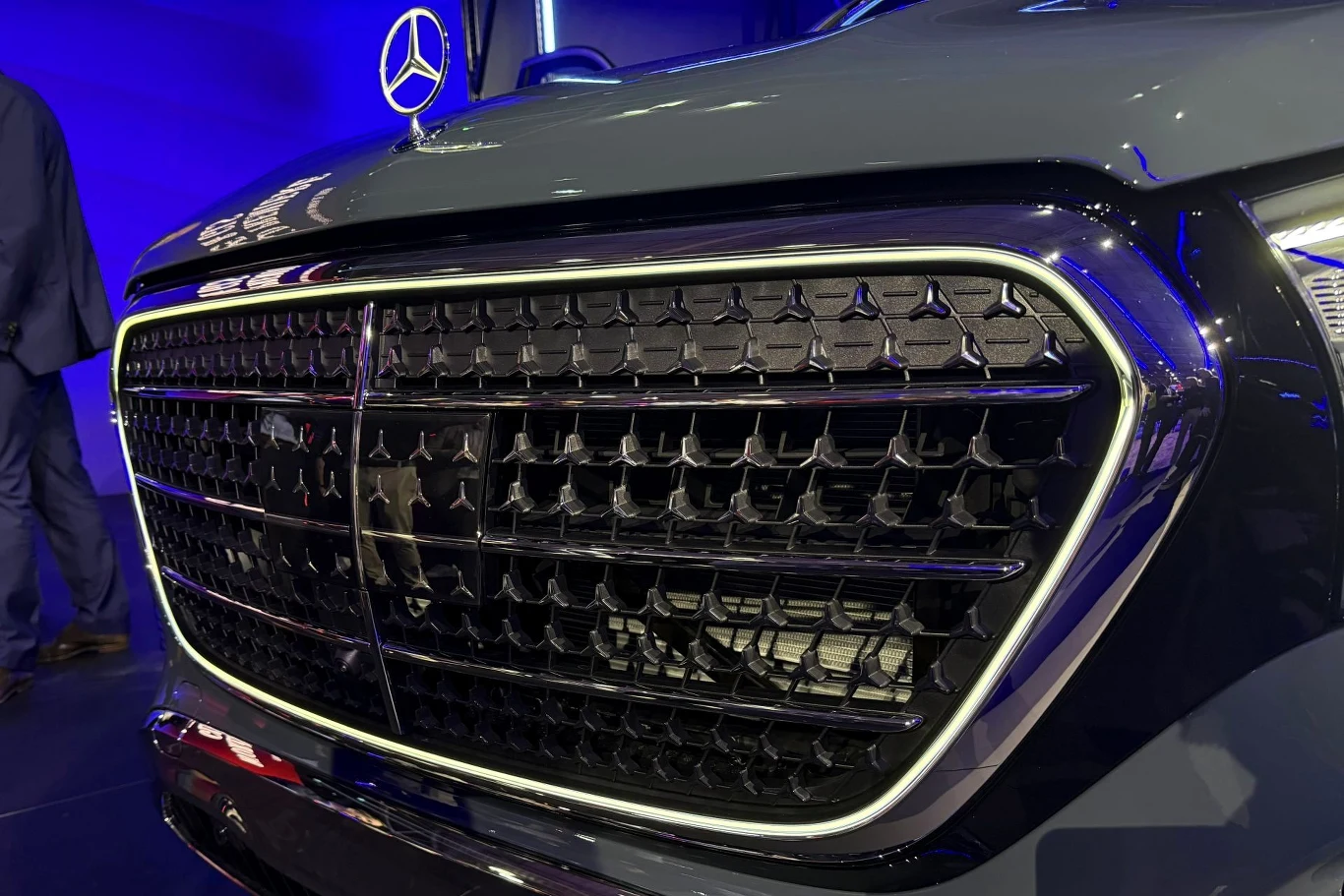 duży, czarny grill z charakterystycznym wzorem i chromowaną ramką na froncie luksusowego samochodu marki Mercedes-Benz, powyżej umieszczone logo producenta