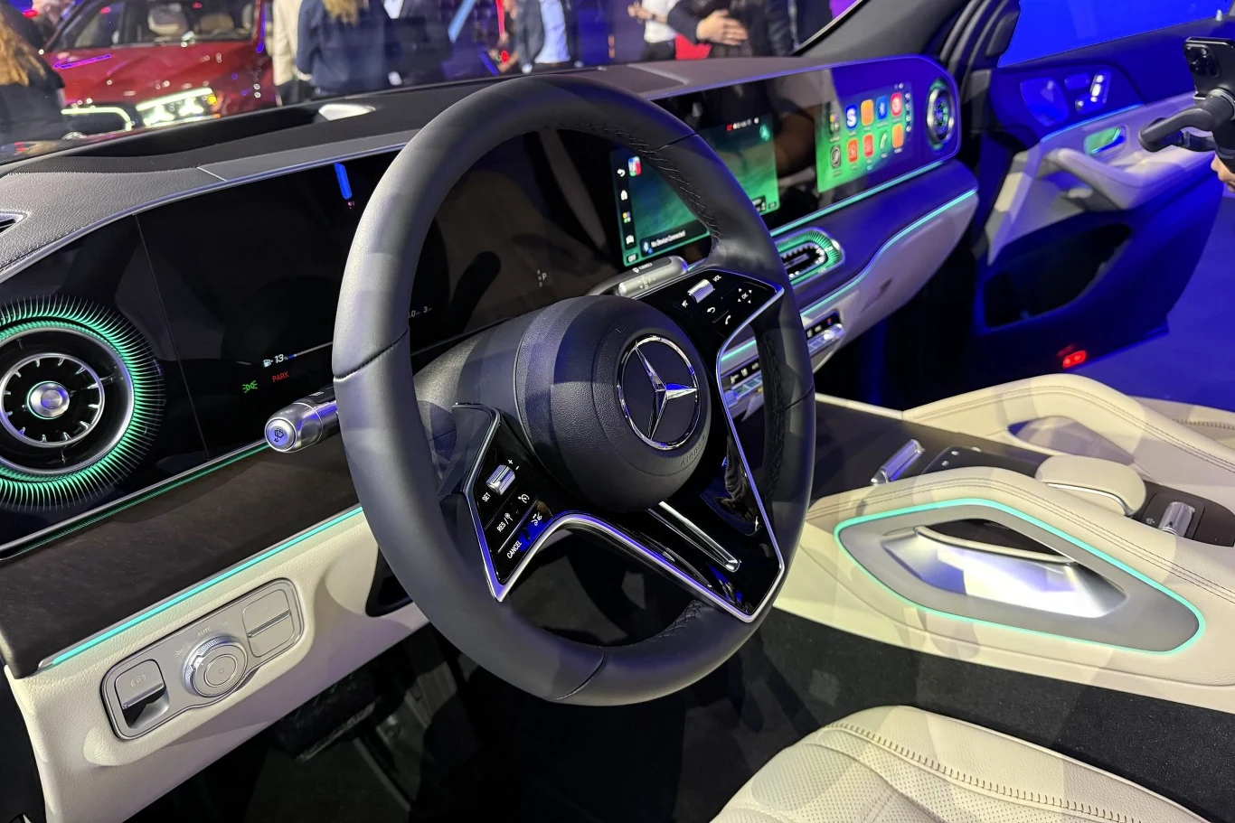 kokpit nowoczesnego samochodu marki Mercedes z dużym, zakrzywionym wyświetlaczem cyfrowym, podświetlaną deską rozdzielczą, stylową wielofunkcyjną kierownicą i jasnymi, skórzanymi fotelami
