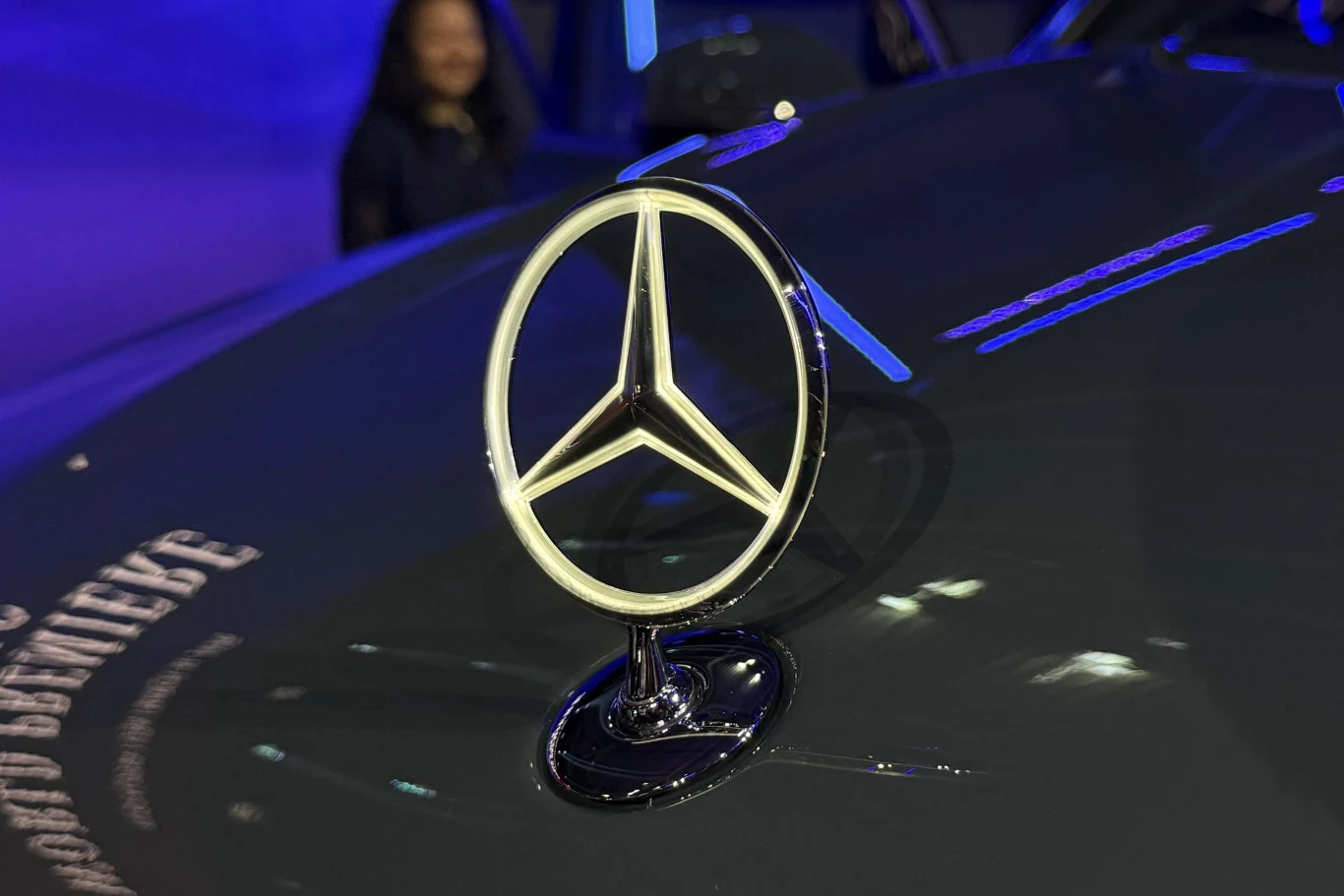 chromowany emblemat Mercedesa umieszczony na masce ciemnego samochodu, wyraźnie oświetlony na tle rozmytego, niebieskiego otoczenia