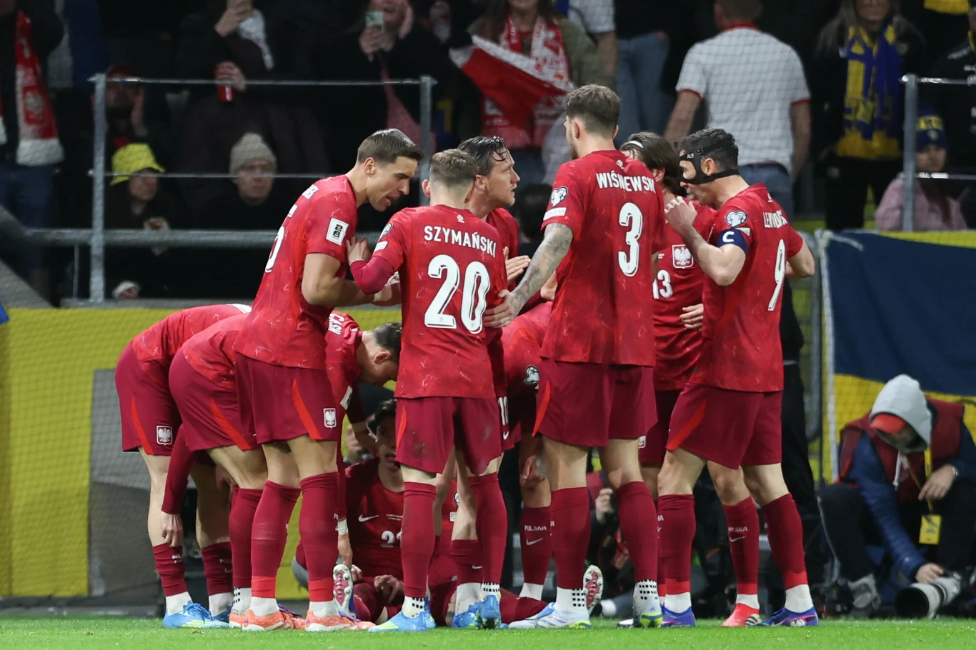 grupa piłkarzy w czerwonych strojach zgromadzona w kole, koncentrująca się i rozmawiająca przed rozpoczęciem meczu na stadionie