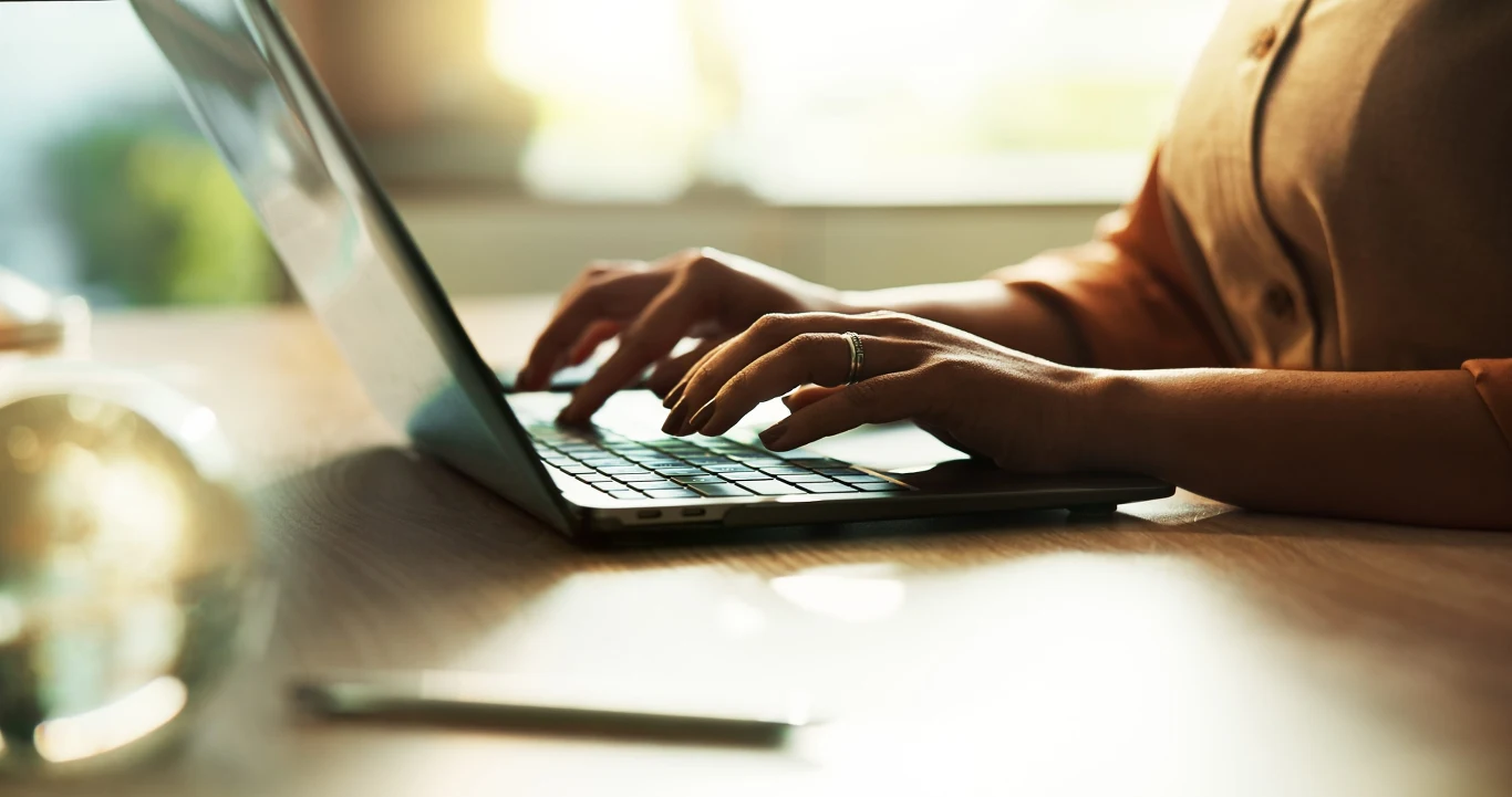 Sklepy internetowe będą musiały udostępnić konsumentom specjalny przycisk z napisem "odstąp od umowy tutaj" Osoba pisze na klawiaturze laptopa; na biurku widoczny długopis, jasne światło; kontekst sklepów online.