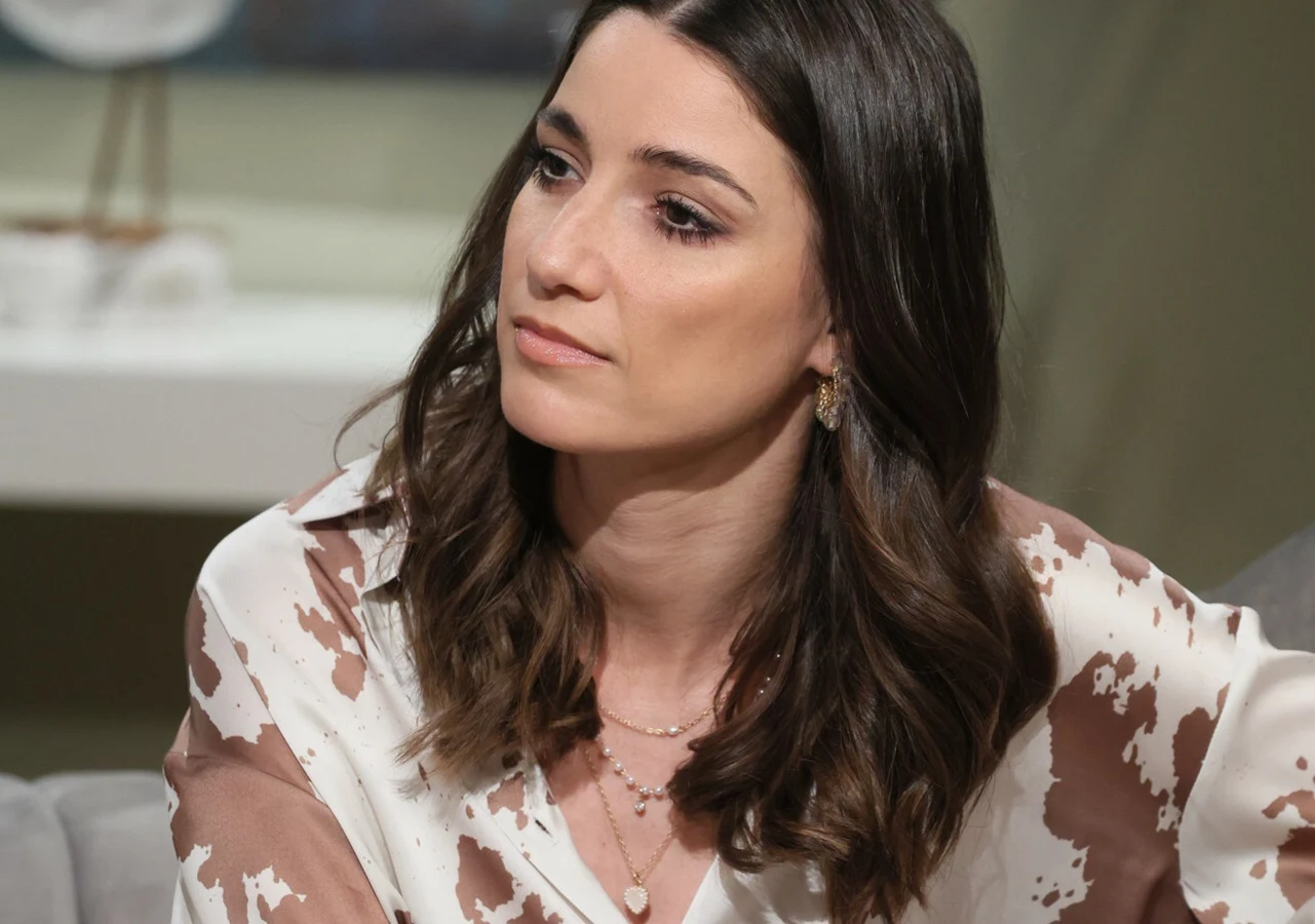 Lenka Klimentova Lenka Klimentova siedzi na sofie, ubrana w białą koszulę z brązowym wzorem, patrzy w bok; w tle jasne wnętrze.