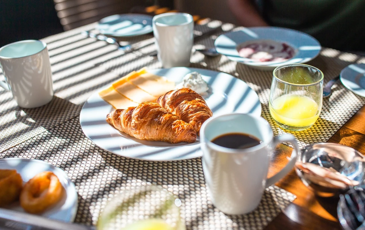 Śniadanie hotelowe Kruasant, ser i masło na talerzu, obok filiżanka kawy i szklanka soku, na stole śniadaniowym w hotelu.