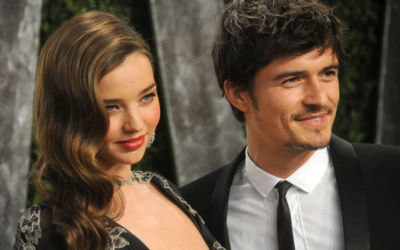 Para elegancko ubranych osób stoi blisko siebie, kobieta ma długie, falujące włosy i efektowny makijaż, mężczyzna ma krótko przycięte włosy i nosi garnitur z krawatem, oboje uśmiechają się w stronę aparatu.