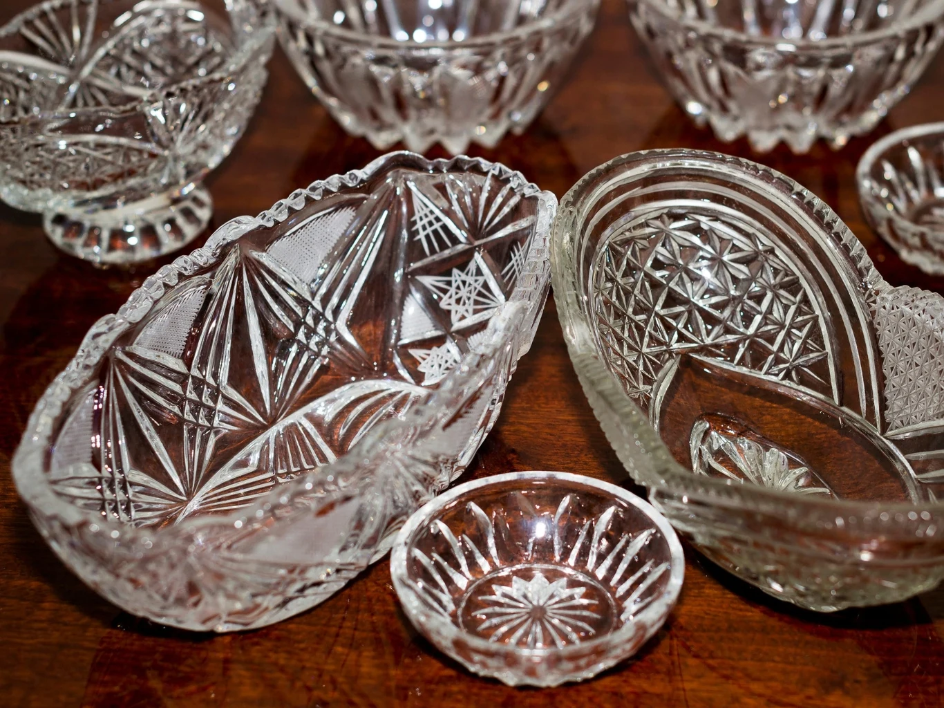 Bogato zdobione kryształowe miseczki i salaterki o różnych kształtach, ustawione na drewnianej półce