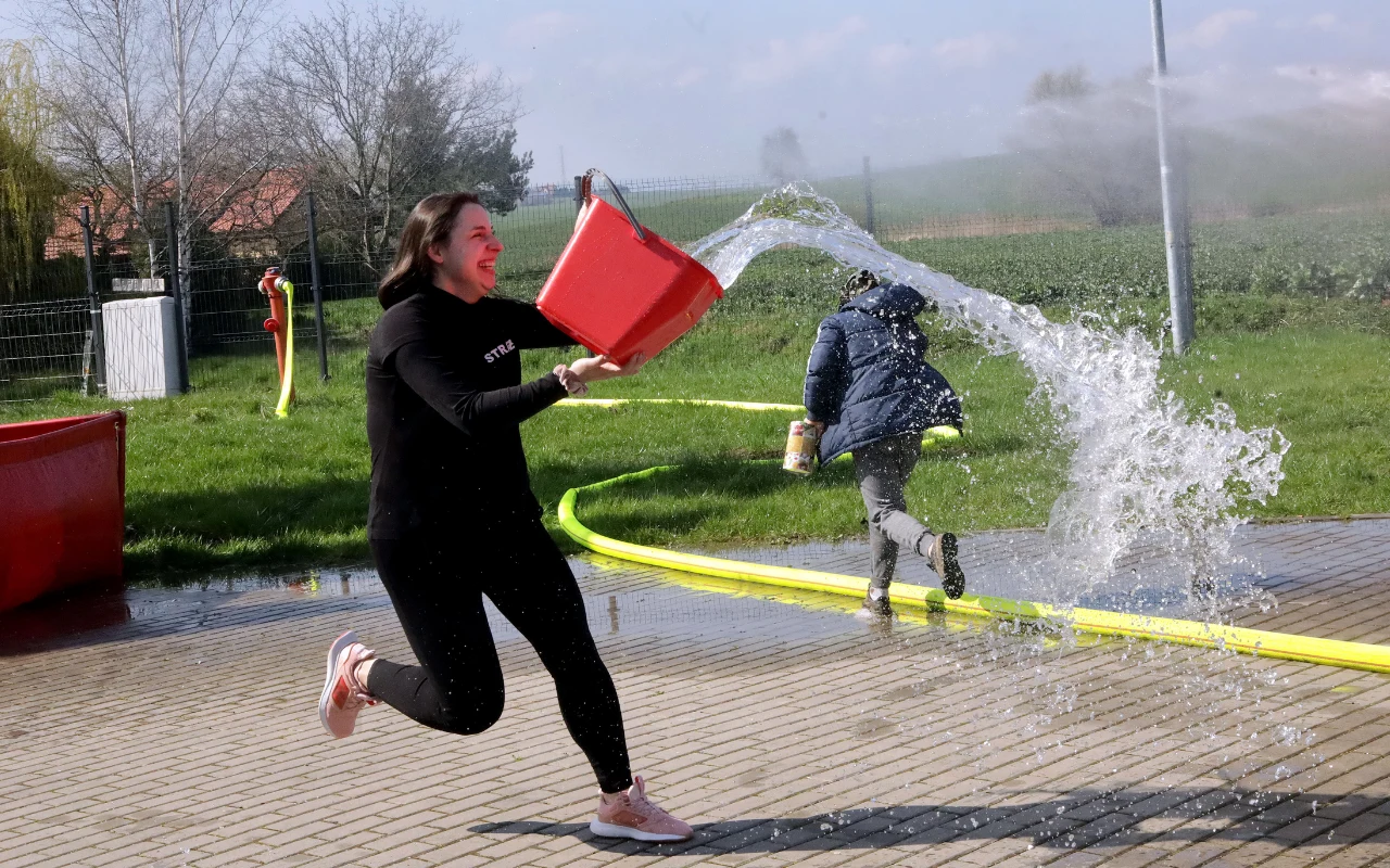 Zwyczaj, który przyciąga szczęście i zdrowie. Pamiętaj o nim w Poniedziałek Wielkanocny. Kobieta z czerwonym wiadrem pełnym wody w lany poniedziałek. Tradycja, która przynosi zdrowie i szczęście.