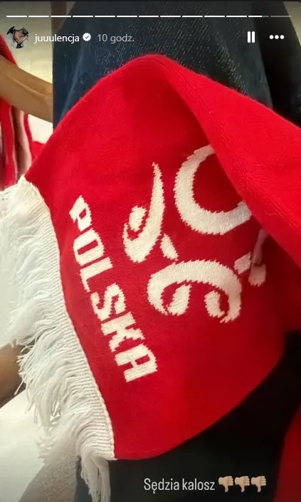 Czerwony szalik z napisem 'POLSKA' i białymi frędzlami leży na udzie osoby ubraną w ciemne spodnie.