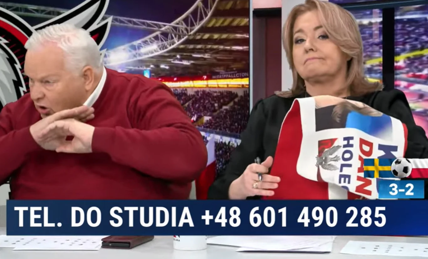 dwoje komentatorów sportowych w studiu telewizyjnym, kobieta trzyma flagę z napisem, mężczyzna wykonuje energiczny gest ręką, w tle stadion piłkarski, na dole plansza z numerem telefonu i wynikiem meczu