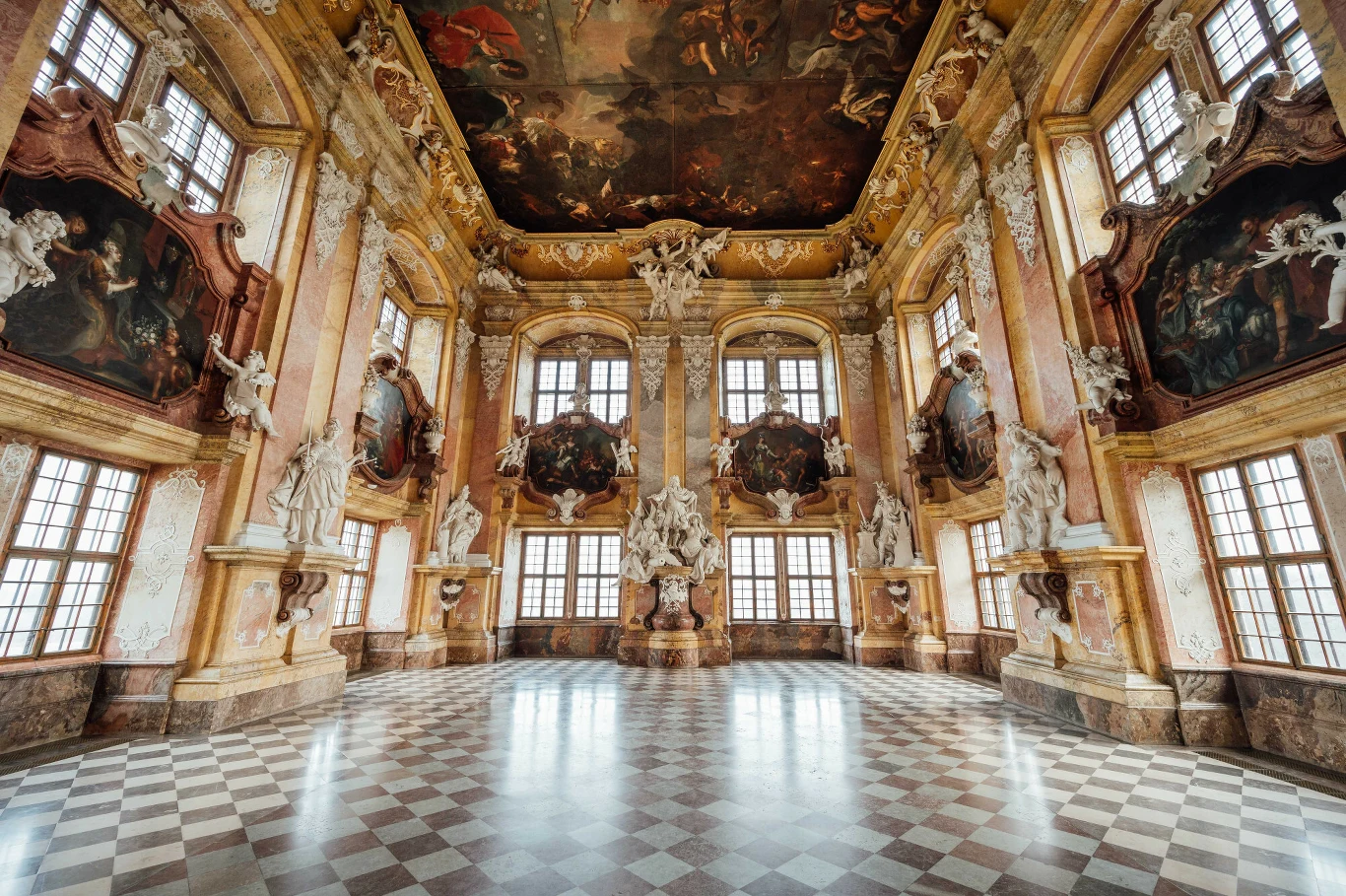 bogato zdobiona sala pałacowa z marmurową posadzką, monumentalnymi rzeźbami, barokowymi zdobieniami, dużymi obrazami umieszczonymi na ścianach i imponującym malowidłem na suficie, przez wysokie okna wpada naturalne światło
