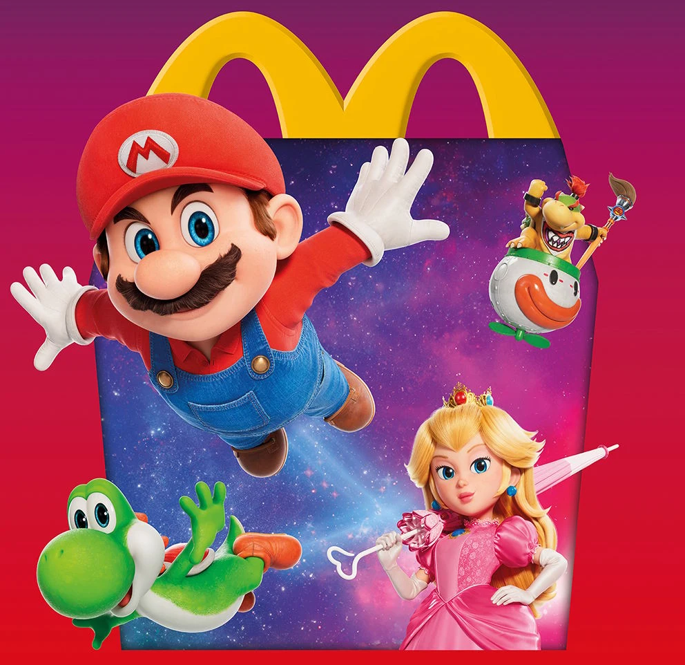 Mario w czerwonej czapce i niebieskich ogrodniczkach wyskakuje na pierwszy plan, towarzyszą mu zielony Yoshi, księżniczka Peach w różowej sukni z parasolką oraz Bowser Jr. unoszący się w maszynie bojowej, wszystko na tle kolorowego pudełka Happy Meal z...