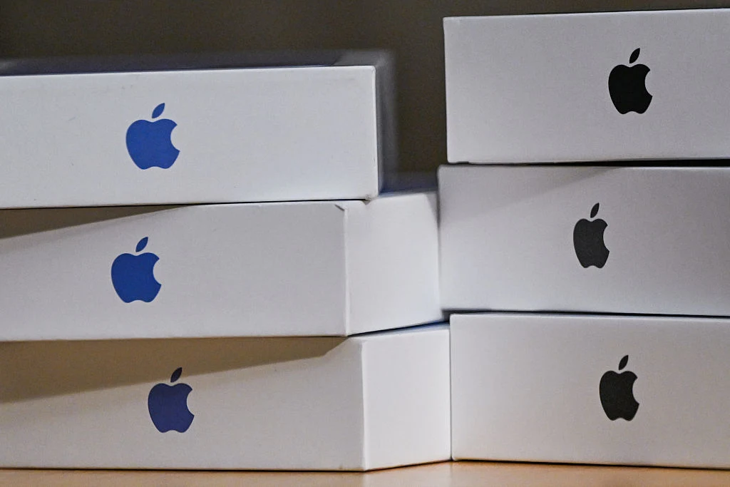 stos białych pudełek z charakterystycznym logo Apple w kolorze czarnym i niebieskim, ułożonych jeden na drugim na jasnej powierzchni