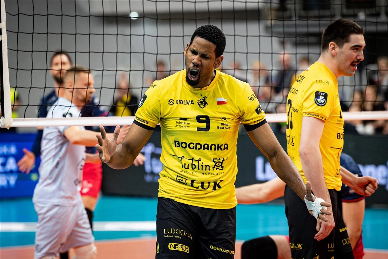 siatkarz w żółtej koszulce z numerem 9 wyraża silne emocje po zdobyciu punktu podczas meczu, obok niego inni zawodnicy w tle, a po drugiej stronie siatki siatkarz drużyny przeciwnej