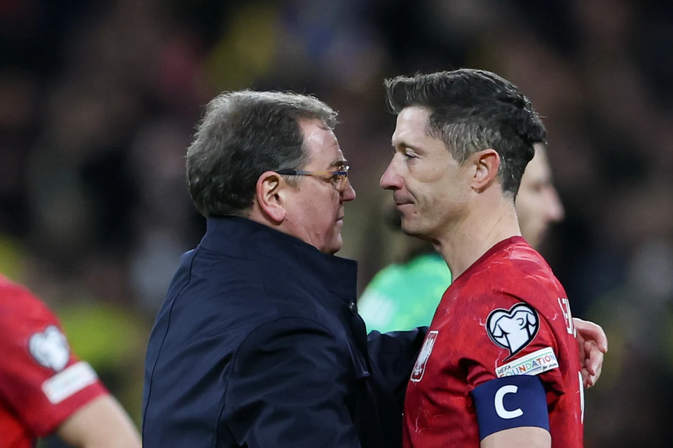 trener obejmuje zawodnika w czerwonej koszulce z opaską kapitana, obaj patrzą sobie w oczy, atmosfera pełna emocji i powagi