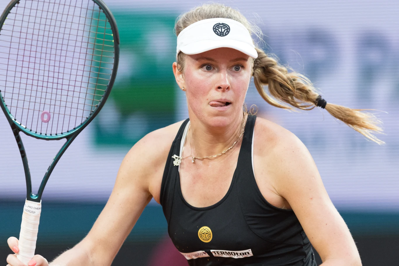 Magdalena Fręch Kobieta grająca w tenisa, ubrana w czarną koszulkę sportową i białą czapkę z daszkiem, skupiona w trakcie meczu, z rakietą tenisową w dłoni.