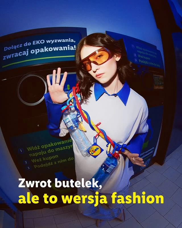 Młoda osoba w okularach przeciwsłonecznych ubrana modnie trzyma kilka pustych plastikowych butelek przyczepionych do kolorowej liny; w tle automat do zwrotu opakowań i hasło zachęcające do ekologicznego stylu życia.