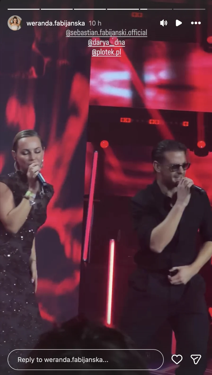 Dwoje wokalistów występujących na scenie w dynamicznym oświetleniu, śpiewających do mikrofonów, ubrani elegancko na tle czerwonych świateł i scenografii koncertowej.