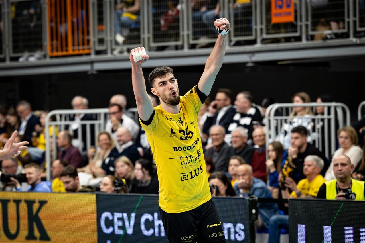 siatkarz w żółtej koszulce drużyny Bogdanka LUK Lublin z uniesionymi w geście triumfu rękami na tle kibiców siedzących na trybunach podczas meczu CEV Champions League