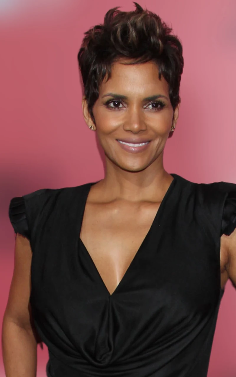 kobieta z krótkimi, ciemnymi włosami, uśmiechnięta, w eleganckiej czarnej sukience na tle jednolitego, różowego tła