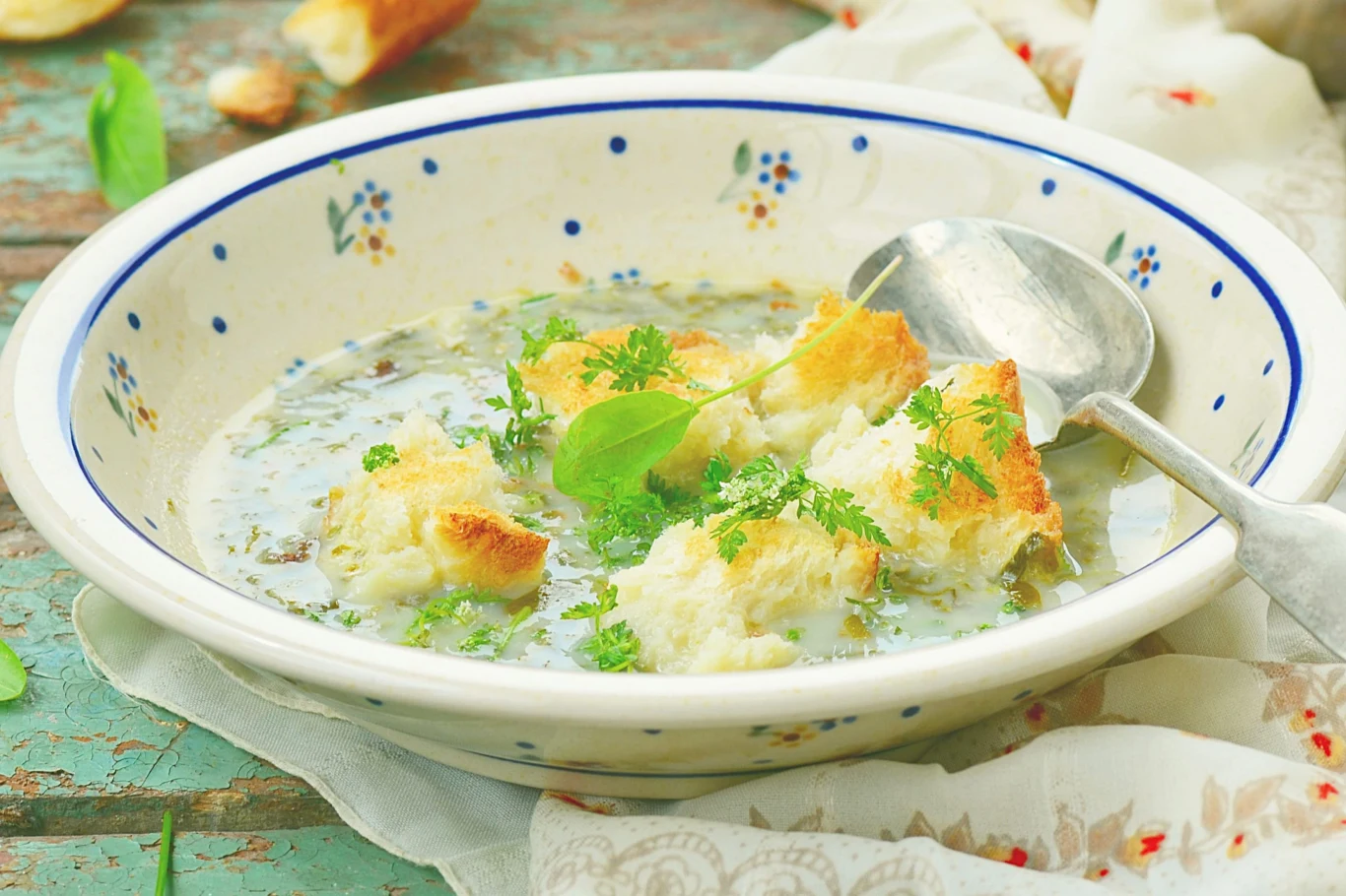 Zupa z pokrzywy to lekki wiosenny obiad Talerz z zupą z pokrzywy, kawałkami pieczywa, świeżymi ziołami oraz metalową łyżką na stole.